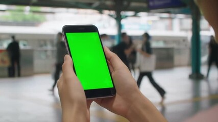 Closeup of a person holding a smartphone with a green screen ideal for chroma key compositing against a blurred background of a busy train station or public transport hub showcasing modern technology. - Powered by Adobe