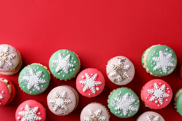 Beautifully decorated Christmas macarons on red background, flat lay. Space for text