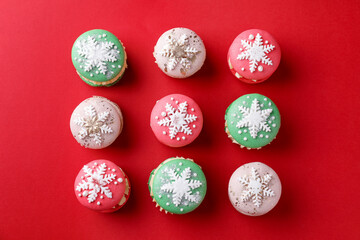 Beautifully decorated Christmas macarons on red background, flat lay