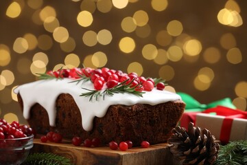 Tasty Christmas cake with red currants, fir branches, cone and gifts on table against blurred festive lights, closeup. Bokeh effect