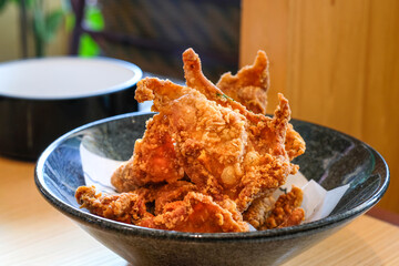 Crispy fried chicken skin served on a black ceramic bowl over a wooden table under natural light. Perfect for restaurant menus, snack product ads, or food blog illustrations