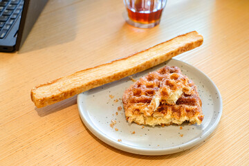 A croffle with cinnamon sugar topping and a slice of garlic bread served on a gray ceramic plate over a wooden table in natural light. Perfect for bakery advertising, cafe menu