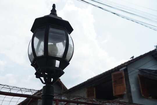 Ornate Vintage Street Lamp Against Cloudy Sky and Old Buildings - Powered by Adobe