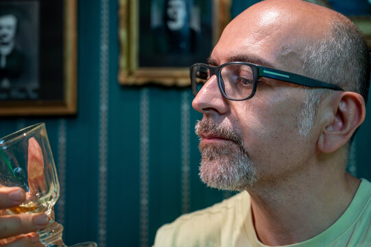 Prague, Czech Republic, August 8, 2023. Portrait of a middle-aged man drinking absinthe, looking into his glass. Relaxation and meditation in a bohemian setting. Artistic lifestyle.