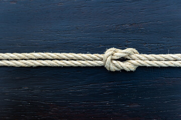 Fototapeta premium Tied rope knot on dark wooden background, symbolizing unity, strength, security, and resilience. Great for business, relationship, or nautical concept visuals and design projects.