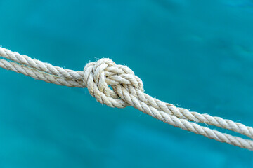 Close-up of a strong rope knot with blue water background, symbolizing connection, strength, security, and teamwork. Ideal for conceptual use in business, safety, or maritime themes.
