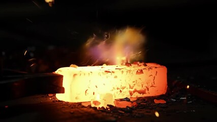 Glowing steel bar heated, ready to shape in dark blacksmith forge, close up; for industrial use