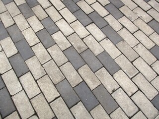 Top-down view of rectangular concrete paving blocks in an alternating gray and light beige color pattern, creating a textured geometric background.