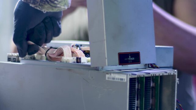 Close-up view of the complex internal structure and ribbon cables of a high-power ASIC miner being repaired. - Powered by Adobe