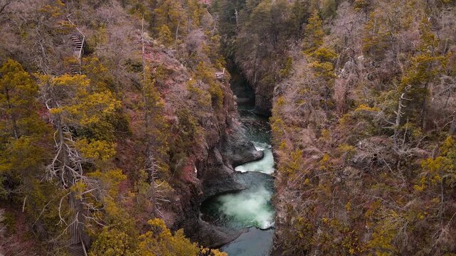 Forward drone aerial of emerald pools through narrow canyon slot, Siete Tazas National Park, &Ntilde;uble, Chile with autumn forest and viewing walkway