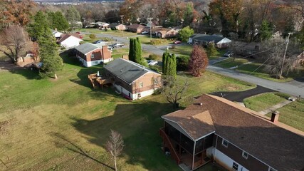 Orbiting drone flight over a quiet American suburban neighborhood in fall, with homes, vibrant trees and streets under clear sunlight, hinting at digital connectivity and sustainable energy themes. - Powered by Adobe