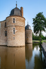 A scenic view of the round tower of Château de Lavaux-Sainte-Anne in Belgium, reflected in the calm waters of the moat on a sunny day, showcasing timeless architecture and serene countryside charm.