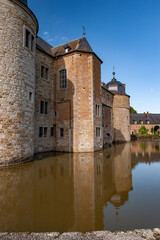 The historic Château de Lavaux-Sainte-Anne reflects in the calm moat waters under a clear blue sky, revealing its fortified stone walls and peaceful Belgian village surroundings.