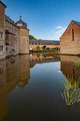 The calm waters surrounding Château de Lavaux-Sainte-Anne reflect its historic stone architecture and blue sky, creating a peaceful scene of medieval heritage in the heart of the Belgian countryside.