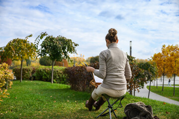 Artist painting outdoors with back view in autumn park.