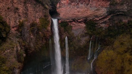 drone aerial of waterfall cascading through narrow canyon slot, Siete Tazas National Park, Ñuble, Chile with dramatic red rock cliffs - Powered by Adobe