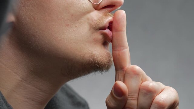 The finger gesture for silence.
A man signals that people should not speak loudly and should remain quiet.
The man touches his index finger to his lips.
Silence, shh, mouth, lips, index finger