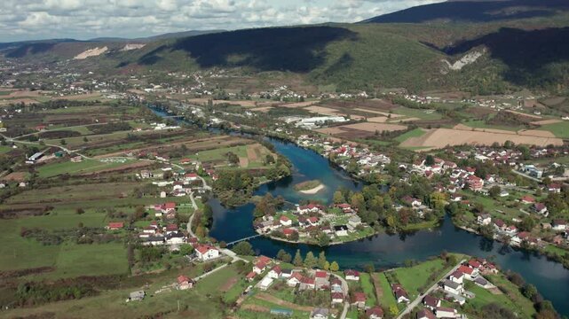 Aerial footage of the Una River meandering through the valley near Bihac, Bosnia and Herzegovina. Scenic rural landscape with fields, houses, and green hills captured in clear daylight.