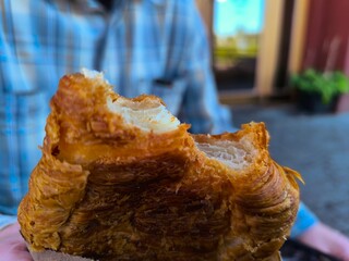 A young man holds a fresh croissant in his hand. Selective focus on his hands against a blurred background.