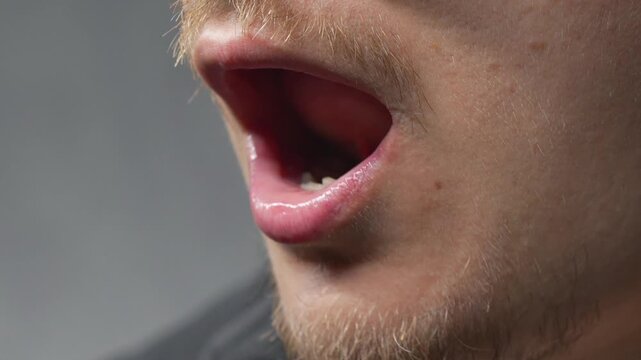 A man sticks his tongue out at the camera against a gray background.
Wet tongue in a man's mouth.
Male facial expression and obscene gesture.