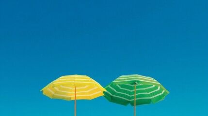 Obraz premium Two vibrant umbrellas stand side by side on a sandy beach, their green and yellow stripes bright against the clear blue sky. A perfect day for fun and relaxation