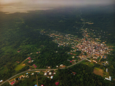Aerial view of a road cutting through the dense forests and a cluster of buildings under a cloudy sunset sky, Tepo, Oti Region, Ghana.