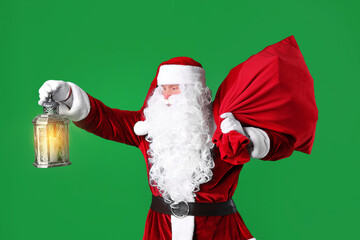 Santa Claus with red bag of Christmas gifts and lantern on green background