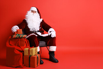 Santa Claus with bag and Christmas gifts on red background, space for text