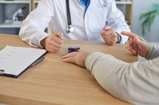 Close up of doctor and senior patient with pulse oximeter on finger having consultation at desk in medical office. Physician explaining treatment plan and monitoring health indicators during visit. - Powered by Adobe
