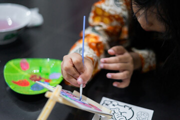 A close-up of a child’s hand painting colorful artwork with a small brush on a canvas. The scene shows bright colors and focused artistic activity.