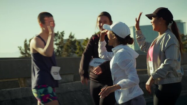 Happy female runners celebrating a fitness achievement with high fives and laughter on an urban bridge. Their camaraderie and success are evident after the race.