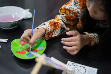 A close-up of a child’s hand painting colorful artwork with a small brush on a canvas. The scene shows bright colors and focused artistic activity.