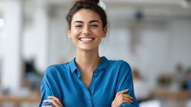 A cheerful Latin American professional stands confidently with arms crossed in a bright office space. Her warm smile radiates positivity and approachability, perfect for a modern workplace