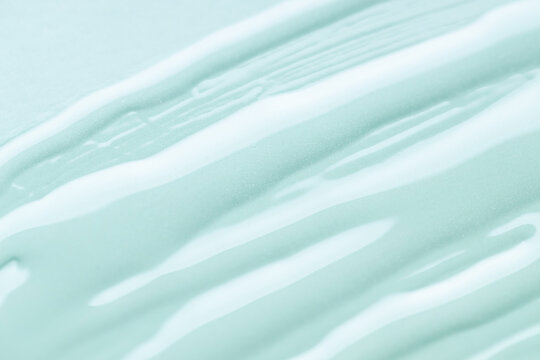 Close-up of flowing aqua liquid streaks on soft mint surface, smooth glossy texture with gentle highlights, clean minimal composition for skincare, cosmetic or wellness themes