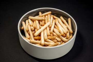 Small breadsticks on white plate on black background