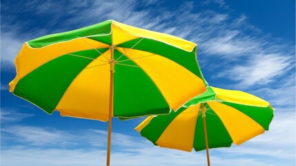 Obraz premium Two vibrant striped umbrellas in shades of green and yellow stand proudly on a sandy beach. The warm sun shines down as gentle waves lap at the shore, creating a serene atmosphere