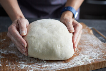 Woman's hands kneading dough on a wooden cutting board.