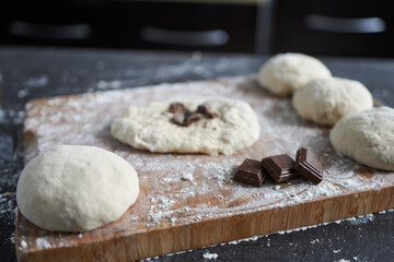 Raw dough and chocolate pieces on a wooden cutting board. Selective focus.
