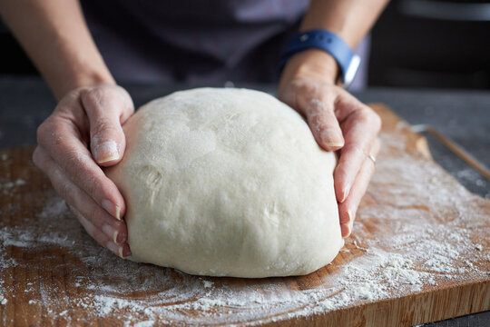 Woman's hands kneading dough on a wooden cutting board.