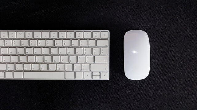 Minimalist top view flat lay of a modern white wireless keyboard and mouse on a black desk mat. Clean workspace concept for remote work, business, technology, or creative design projects