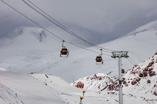 Snow-covered mountains in Kabardino-Balkaria with ski lifts. The landscape features rocky terrain and cloudy skies, creating a winter sports atmosphere.