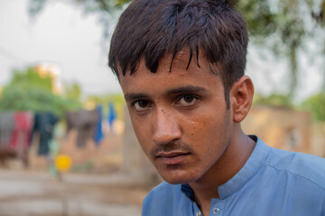 Young rural boy in traditional clothing looking seriously at the camera in a village outdoor setting
