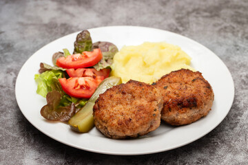 Homemade meat patties served with mashed potatoes and fresh vegetable salad.