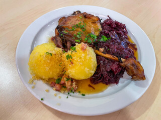 Traditional german dish roasted duck with red cabbage and potato dumplings on the white plate close up