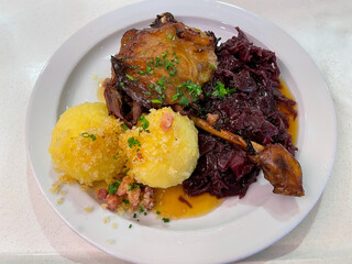 Traditional german dish roasted duck with red cabbage and potato dumplings on the white plate close up