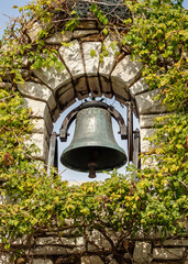 Old bell hanging in a arched opening in a stone wall covered with ivy vines