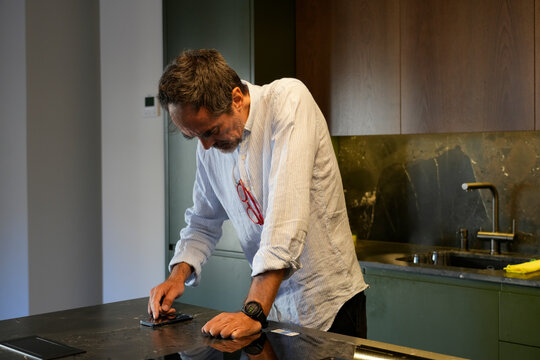 Man cleaning smartphone screen on kitchen counter - Powered by Adobe