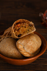 Homemade baked pies (pirozhki) with cabbage in a clay bowl with tea on a wooden table. Traditional Russian, Ukrainian and Belarussian cuisine. Vertical orientation.