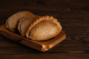 Freshly baked pies on a tray on a wooden table. Russian baked puff pastry with cabbage fillings. Cozy food.