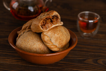 Homemade baked golden pies with apples, pears, and cinnamon made from whole grain flour with cup of tea on a wooden table. Cozy food.